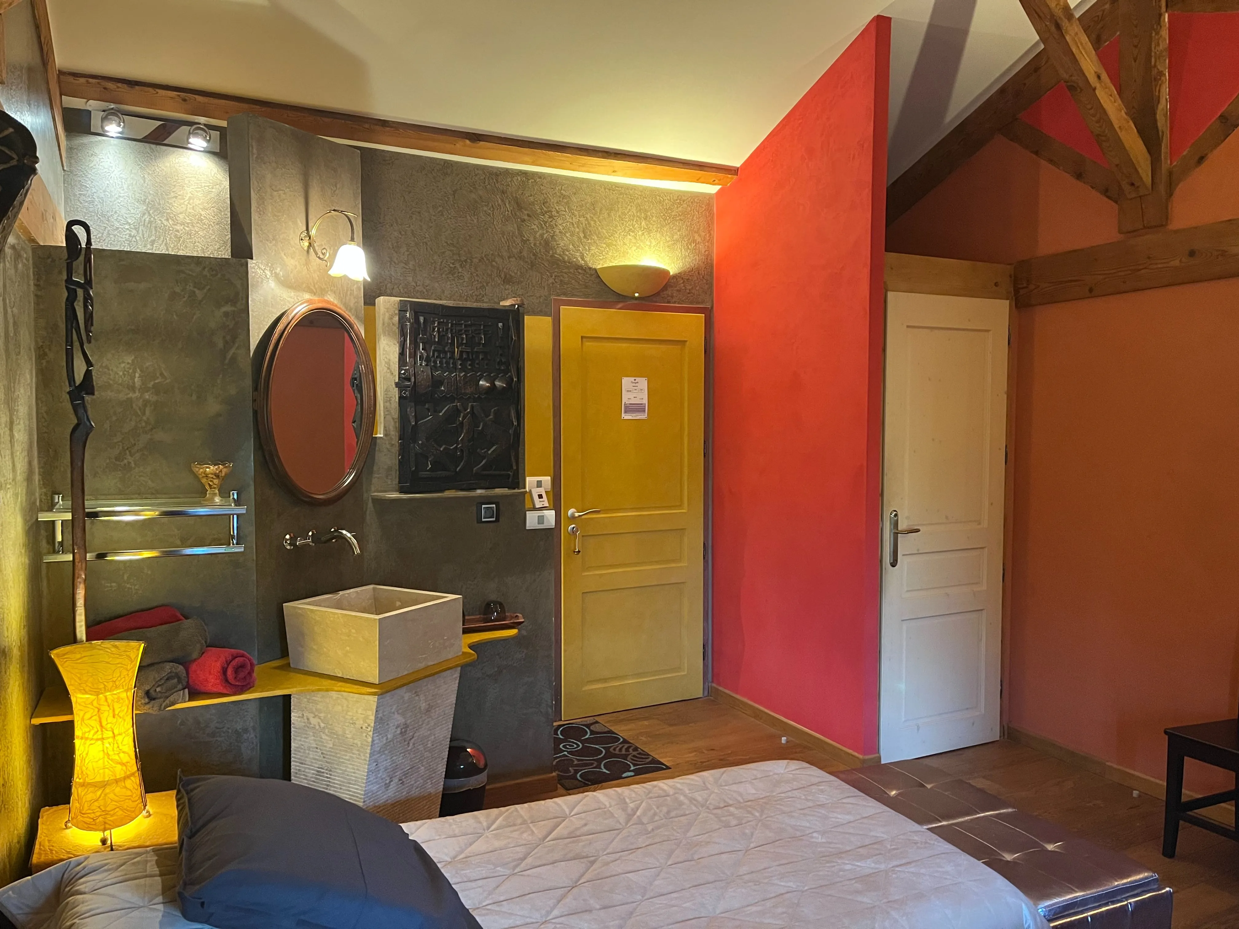 Chambre africaine - Entrée de la chambre avec porte des toilettes à droite et vasque simple avec serviettes disposées à gauche