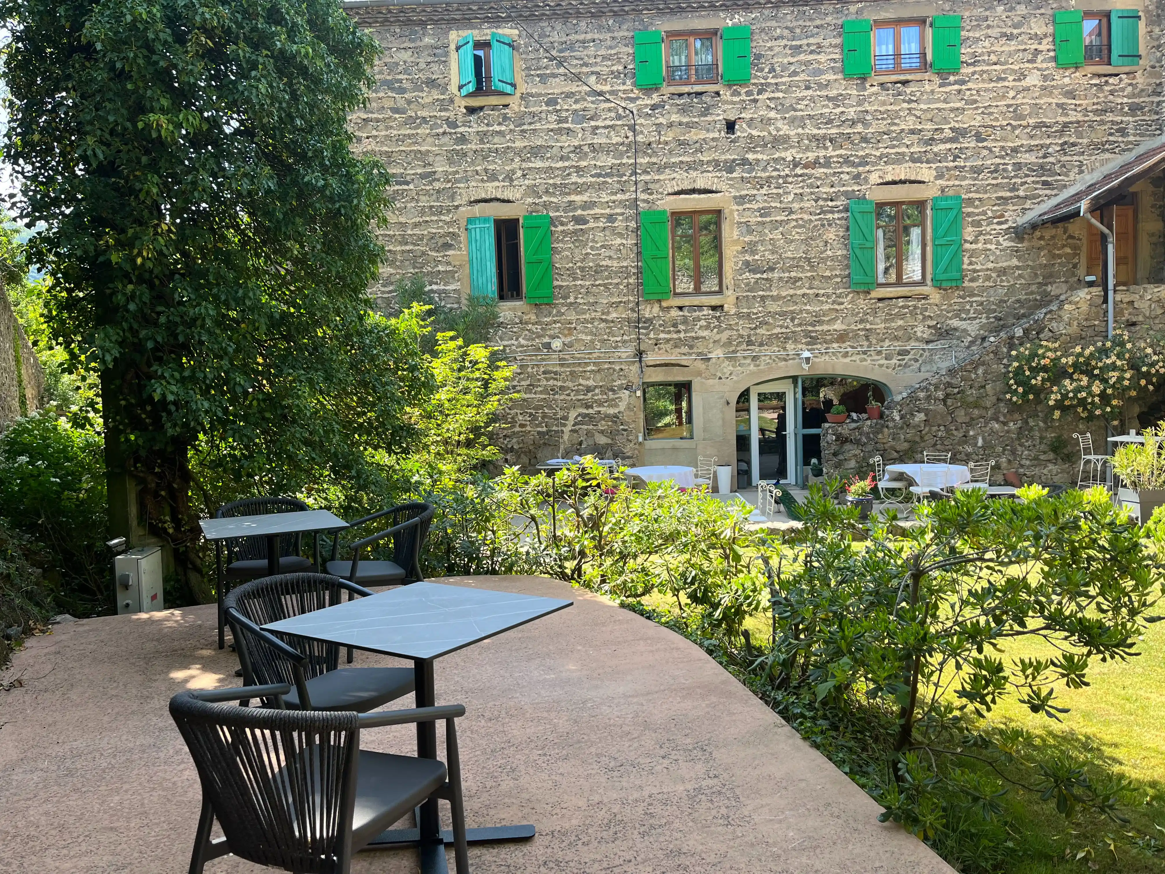 Cour intérieure du Domaine de Pipangaille avec tables et chaises, vue sur la façade en pierre aux volets verts.