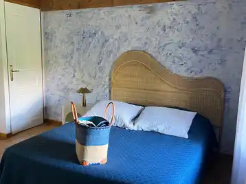 Chambre créole - Grand lit double avec panier de serviettes au pied du lit et porte des toilettes en arrière-plan