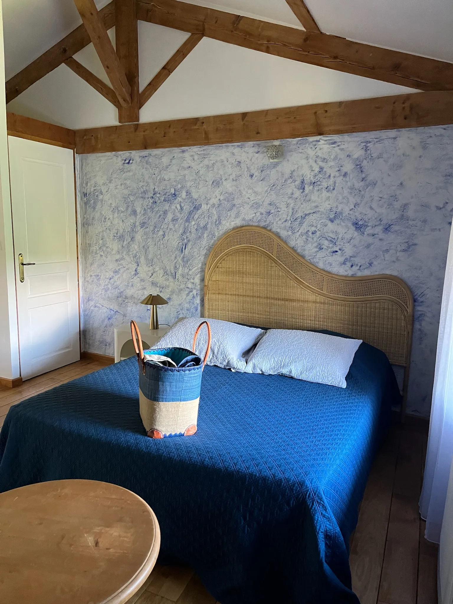 Chambre créole - Grand lit double avec panier de serviettes au pied du lit et porte des toilettes en arrière-plan