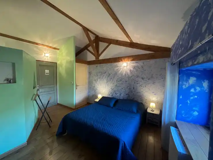 Chambre créole - Vue d’ensemble de la chambre bleue avec lit double, lampe de chevet allumée et fenêtre ouverte sur le jardin