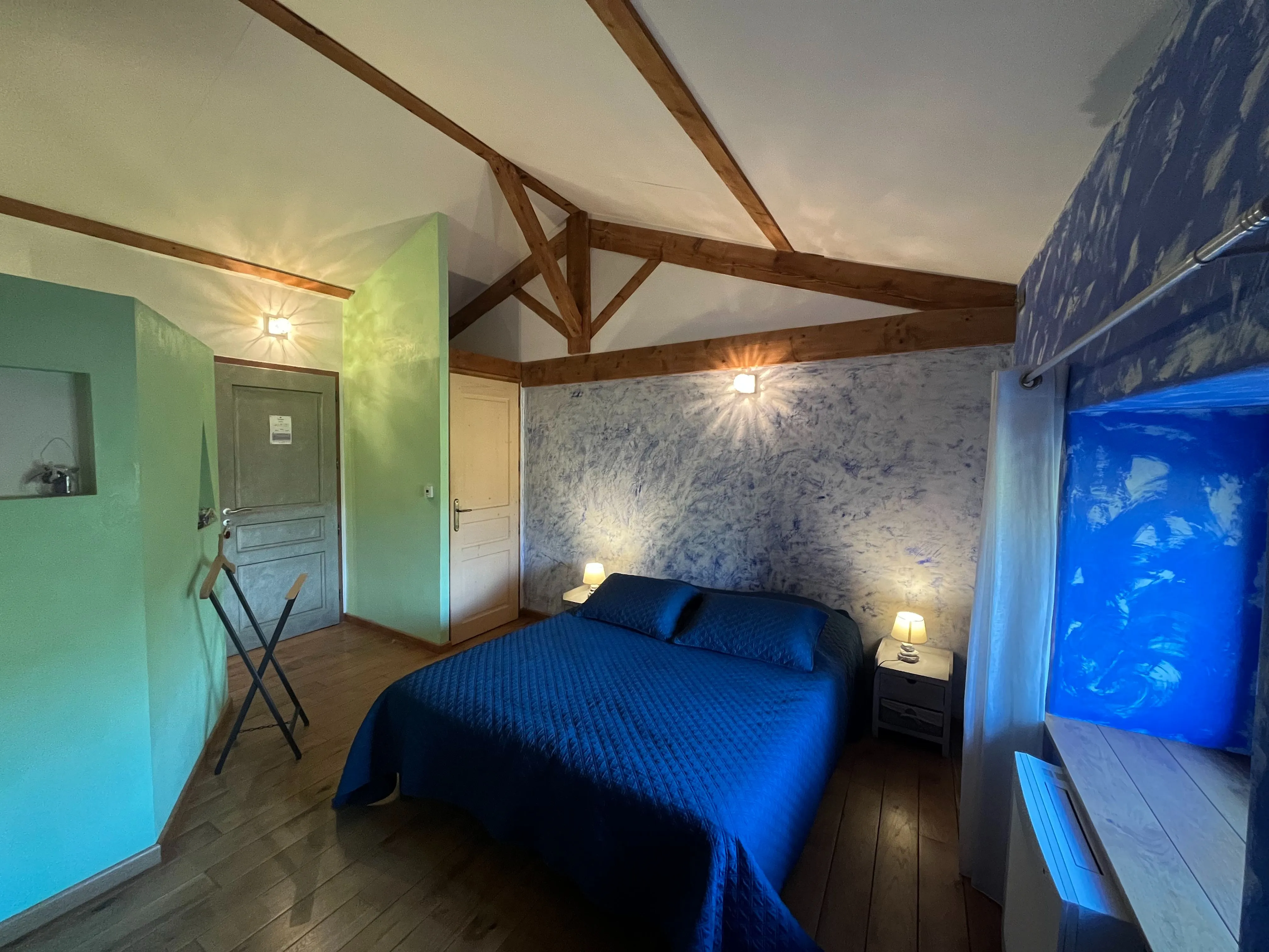 Chambre créole - Vue d’ensemble de la chambre bleue avec lit double, lampe de chevet allumée et fenêtre ouverte sur le jardin