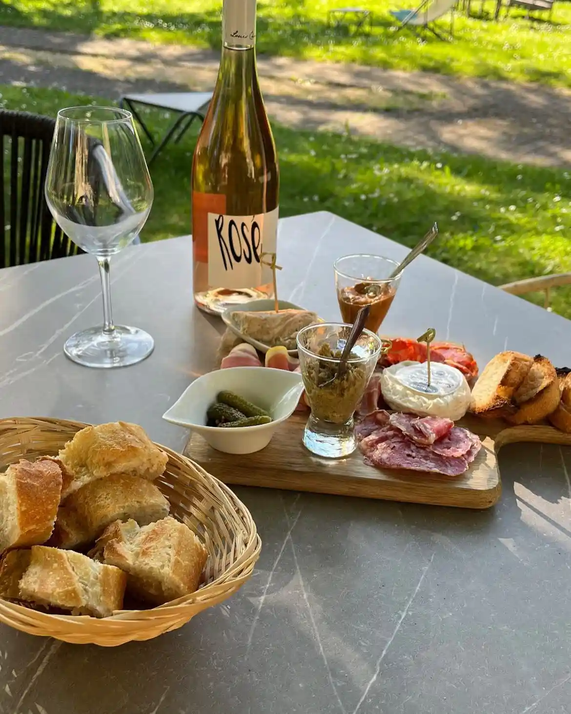 Planche de charcuterie et fromages accompagnée de pain grillé, cornichons et verre de rosé