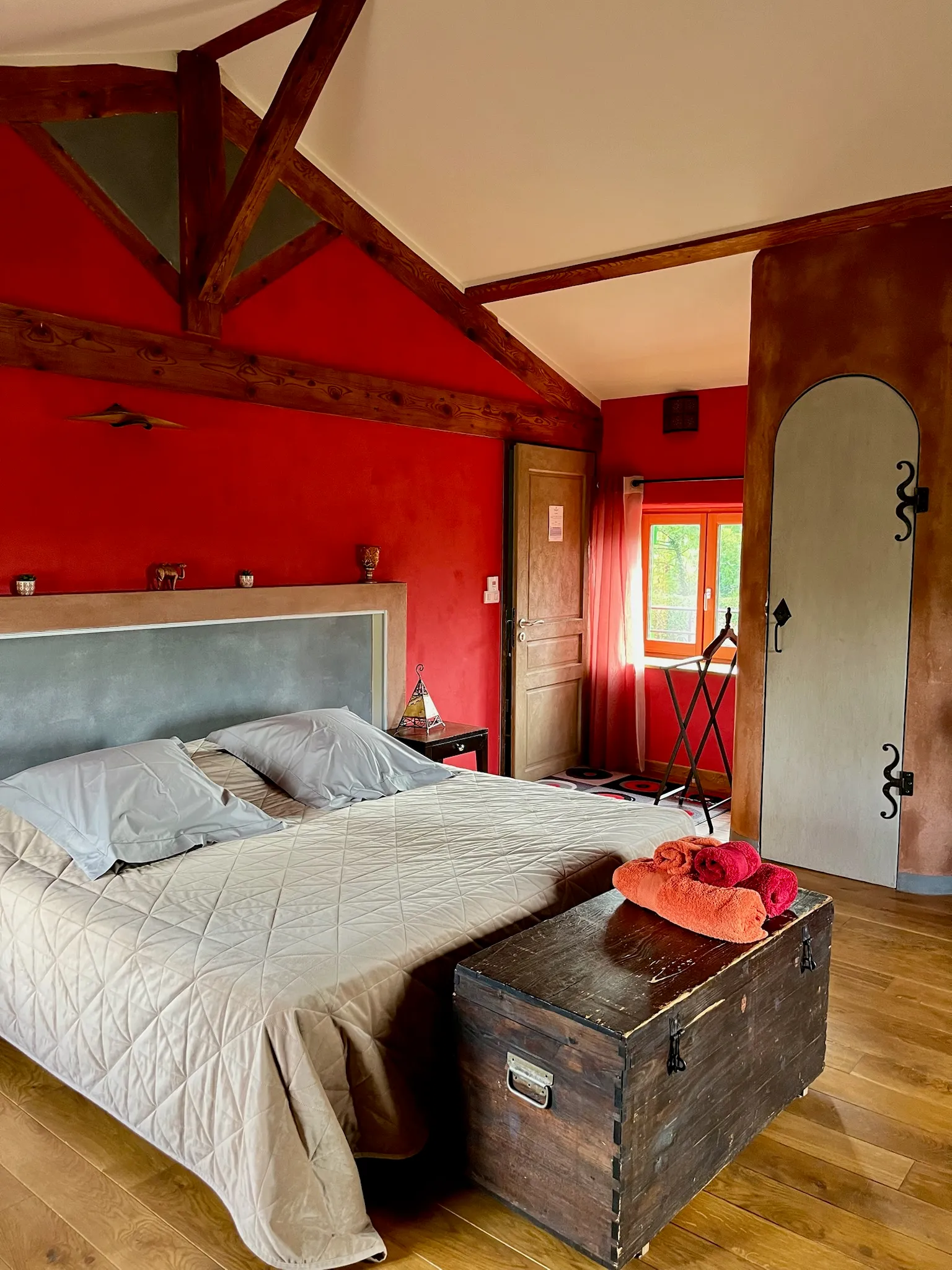 Suite marocaine - Lit double vu de côté avec porte de la chambre, fenêtre sur cour et serviettes disposées sur le coffre au pied du lit