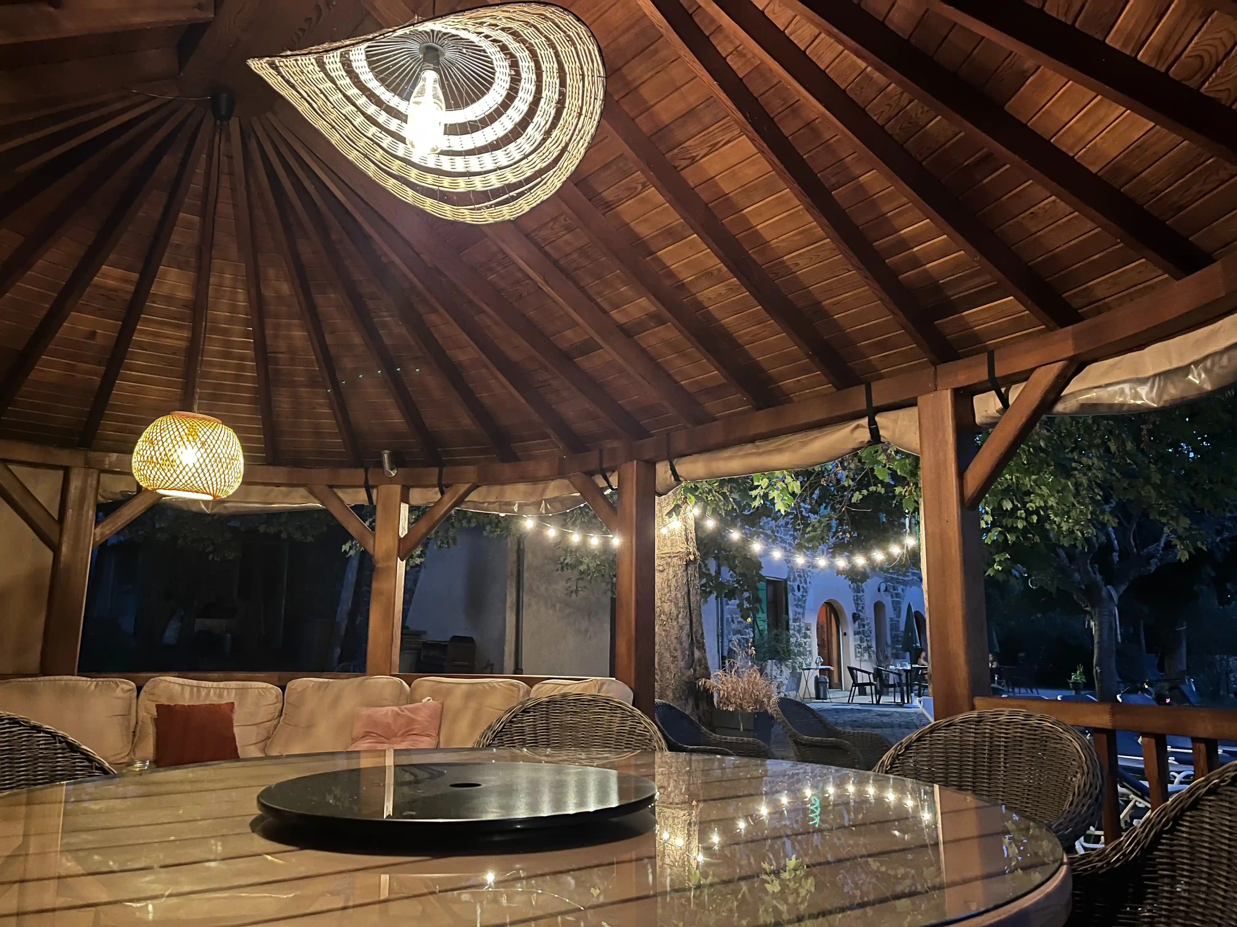 Pavillon près de la piscine avec grande table et espace salon éclairé par des guirlandes lumineuses