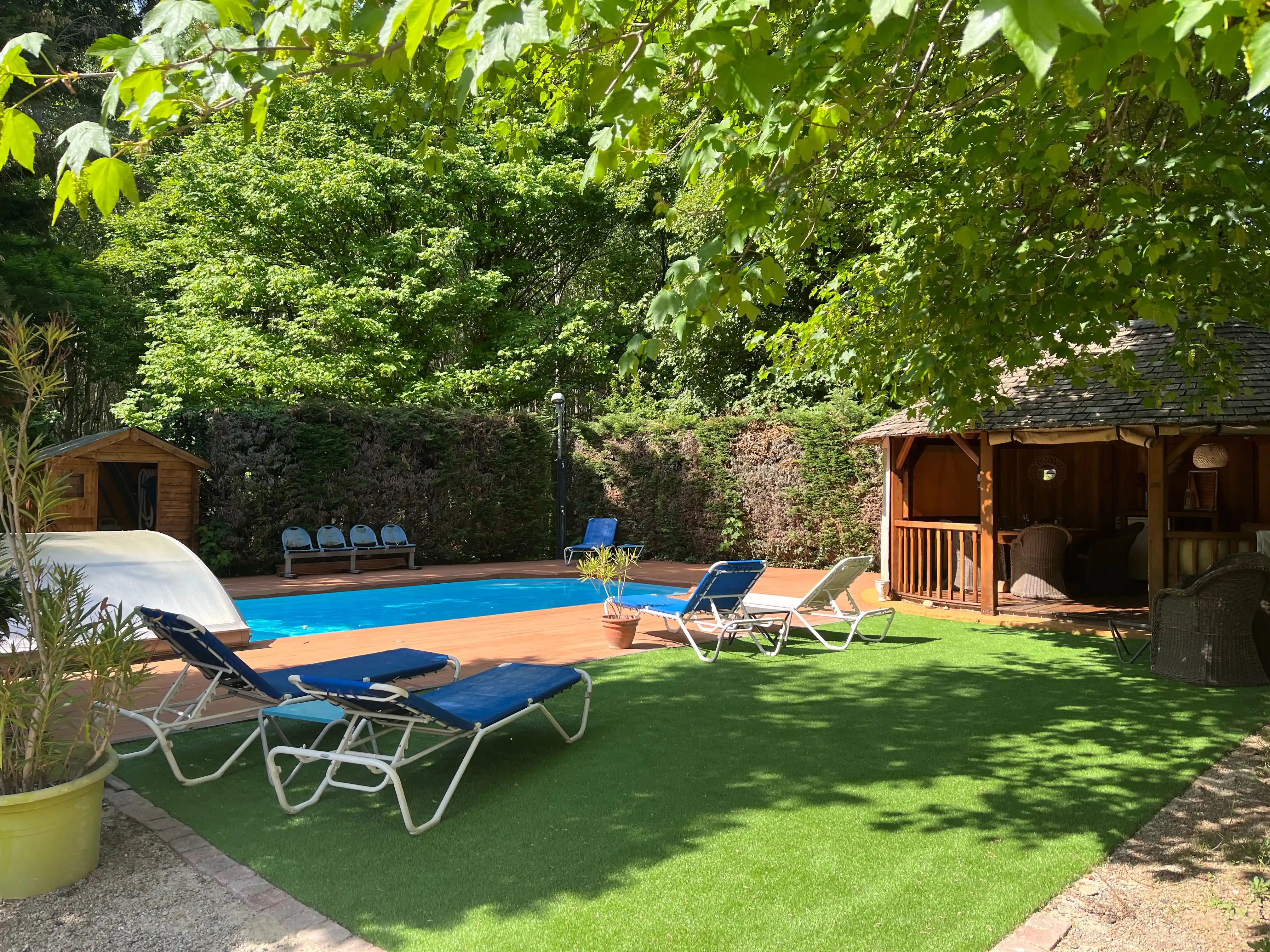 Piscine extérieure entourée de transats et végétation avec pavillon en bois à proximité