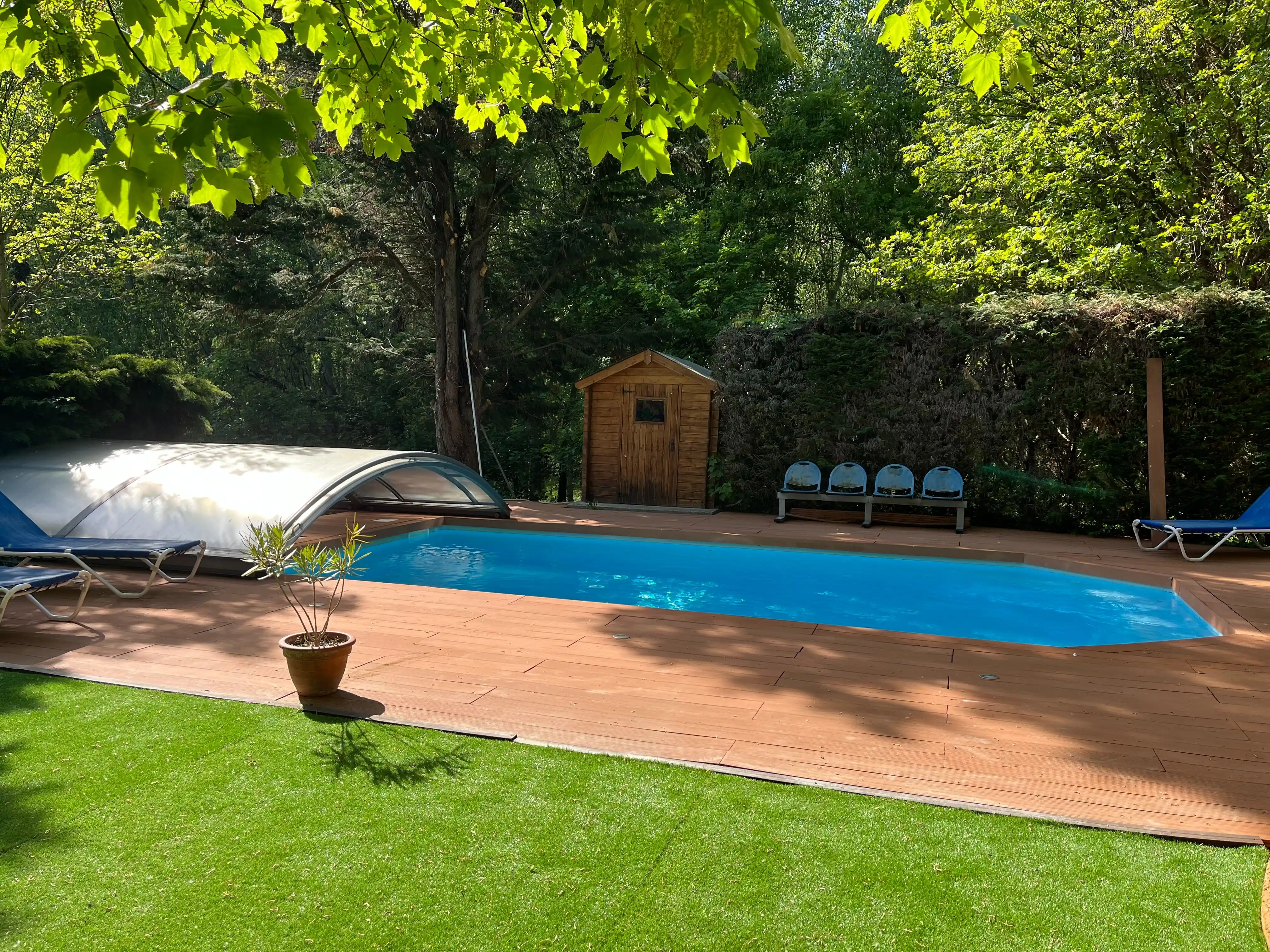 Piscine extérieure du Domaine de Pipangaille entourée d'arbres, avec terrasse en bois et espace en gazon synthétique.