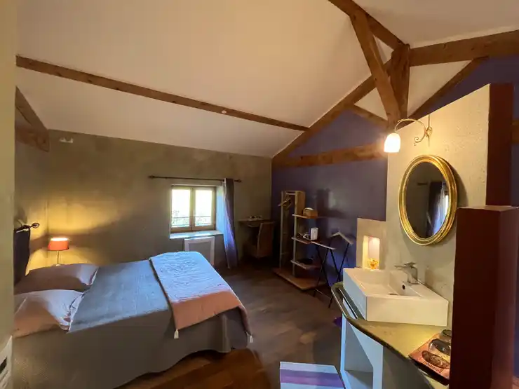 Chambre toscane - Vue d’ensemble de la chambre avec lit double et lampe de chevet allumée, espace de rangement et bureau, vasque simple avec miroir éclairé et fenêtre ouverte sur le jardin